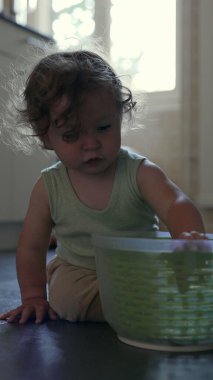 Yürüyen çocuk yerde oynarken kameraya doğru yeşil dönen kaseyi kaldırıyor, oyuncu mutfak aktivitesi sırasında dairesel tasarım ve dokuyu ortaya çıkarıyor