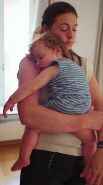 Anne kucağında uyuyan bir bebek, pencerenin yanında, doğal ışık sessiz bir anda huzurlu bir kucaklaşmayla parıldıyor.