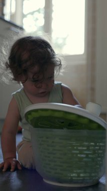 Yürüyen çocuk yerde oynarken kameraya doğru yeşil dönen kaseyi kaldırıyor, oyuncu mutfak aktivitesi sırasında dairesel tasarım ve dokuyu ortaya çıkarıyor