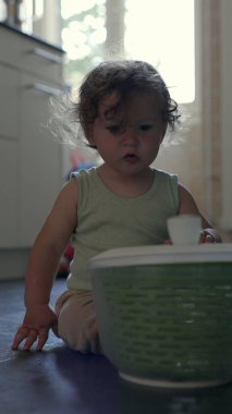 Yürüyen çocuk yerde oynarken kameraya doğru yeşil dönen kaseyi kaldırıyor, oyuncu mutfak aktivitesi sırasında dairesel tasarım ve dokuyu ortaya çıkarıyor