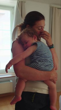 Annem hafifçe aydınlatılmış odada duruyor kıvırcık saçlı bebekle, her iki gözün de dinlenme ve bağlanma anında kapalı.