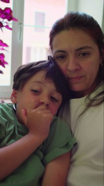 Anne ve oğul birlikte oturup kitap okurken kucaklaşıyorlar, evde sessiz bir hikaye anlatma zamanı boyunca odaklanmış anları paylaşıyorlar.