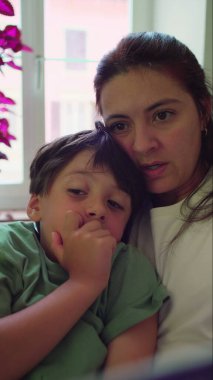 Anne ve oğul birlikte oturup kitap okurken kucaklaşıyorlar, evde sessiz bir hikaye anlatma zamanı boyunca odaklanmış anları paylaşıyorlar.