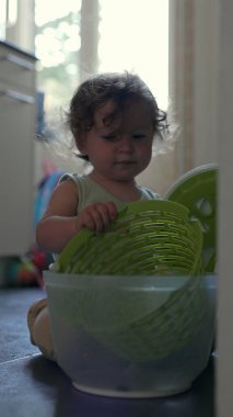 Yürüyen çocuk yerde oynarken kameraya doğru yeşil dönen kaseyi kaldırıyor, oyuncu mutfak aktivitesi sırasında dairesel tasarım ve dokuyu ortaya çıkarıyor