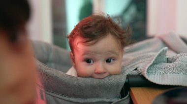 Meraklı yüz ifadesine sahip bebeğe yakın çekim, yüksek sandalyede dinlenme, nazik bakış ve rahat duruş, çevreyi gözlemleme, yumuşak ve özenli, bebeğin yüzüne odaklanma