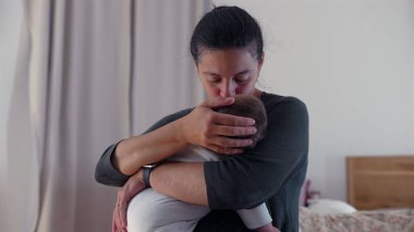 Anne bebeğinin başını öperken, huzurlu bir yuvada bir anlık şefkat ve şefkat içinde bebeğini kucaklar.