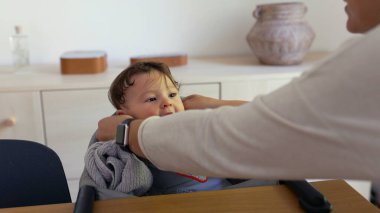 Anne bebeğin etrafına önlük takıyor, nazik bakım, beslenme hazırlığı, ev ortamı, ebeveyn-çocuk etkileşimi, sıcaklık ve rahatlık, günlük aile anları.