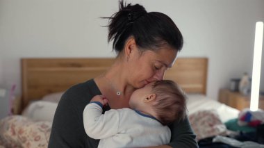 Anne bebeğini alnından öperken kucaklıyor, huzurlu bir evde sevgi ve sevgi dolu bir anı kucaklıyor.