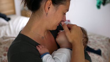 Anne bebeğini kucağında tutuyor, gözleri kapalı, şefkat dolu bir anı kucaklıyor ve sevgi dolu bir evde yaşıyor.