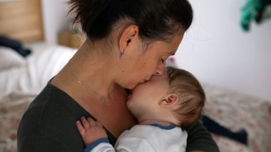 Anne bebeğini kucağında tutuyor, gözleri kapalı, şefkat dolu bir anı kucaklıyor ve sevgi dolu bir evde yaşıyor.