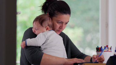 Anne bebeğini masada yazarken kucağında tutuyor, sakin ve besleyici bir ofis ortamında işini tamamlamaya odaklanıyor, bakımı verimlilikle dengeliyor.