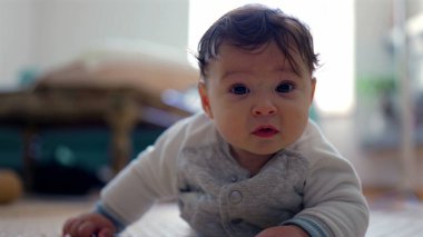 Bebek başını kaldırıyor ve ileriye bakıyor, odaklanmış ifade, elleri destekleyen vücut, erken emekleme aşaması, güç gelişimi, dikkatli bebek içeride, ev ortamında