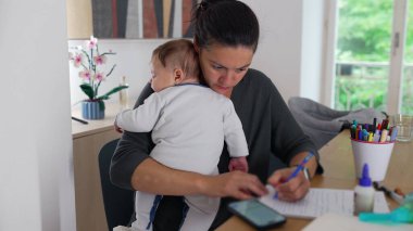 Anne, akıllı telefon kullanarak bebeğini kucağında tutuyor ve masa başında notlar alıyor. Bakıcılık görevini tamamlamaya odaklanırken aynı zamanda ev idaresini de dengeliyor.
