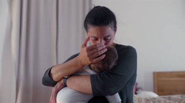 Anne bebeğinin başını öperken, huzurlu bir yuvada bir anlık şefkat ve şefkat içinde bebeğini kucaklar.