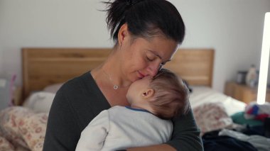 Anne bebeğini alnından öperken kucaklıyor, huzurlu bir evde sevgi ve sevgi dolu bir anı kucaklıyor.
