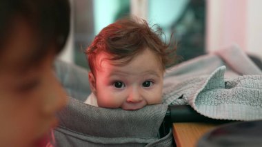 Meraklı yüz ifadesine sahip bebeğe yakın çekim, yüksek sandalyede dinlenme, nazik bakış ve rahat duruş, çevreyi gözlemleme, yumuşak ve özenli, bebeğin yüzüne odaklanma