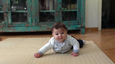 Karnının üstünde bebek, yerde yatarken, erken hareket becerilerini geliştiriyor, başını kaldırıyor, tuhaf bir ifade takınıyor, bebeğin gelişimine odaklanıyor.