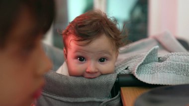 Meraklı yüz ifadesine sahip bebeğe yakın çekim, yüksek sandalyede dinlenme, nazik bakış ve rahat duruş, çevreyi gözlemleme, yumuşak ve özenli, bebeğin yüzüne odaklanma