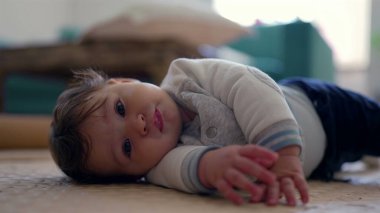 Bebek yan yatmış, başını eğiyor ve gülümsüyor, rahat ve neşeli bir ifade, ev dekorasyonu, erken gelişim aşaması, neşeli ve meraklı bebek içeriyi keşfediyor.