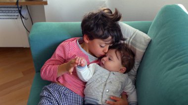 Ağabeyi bebeğin başını öperken kucağında bebek vardı. Kardeşler sessiz ve sevgi dolu bir anın tadını çıkarıyordu. Ev ortamında derin bir bağ ve sevgi.