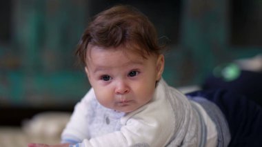 Bebek karnındayken başını kaldırıyor, kameraya meraklı bir ifadeyle bakıyor, erken motor becerileri ile meşgul, rahat bir kıyafet giyiyor.