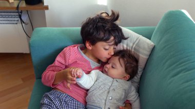 Ağabeyi bebeğin başını öperken kucağında bebek vardı. Kardeşler sessiz ve sevgi dolu bir anın tadını çıkarıyordu. Ev ortamında derin bir bağ ve sevgi.