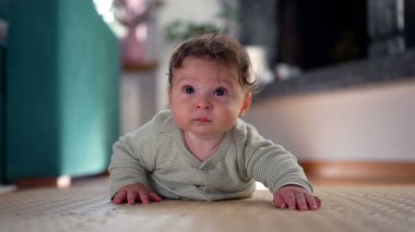 Mindere uzanmış bebek, merakla ve dikkatle çevreyi gözlemliyor, çevreyi keşfederken başını kaldırıyor, kapalı alanlarda erken gelişim faaliyetlerine girişiyor.