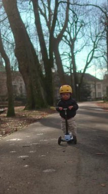 Genç çocuk, uzun ağaçların ve bankların yanında asfalt yol boyunca yolculuk eder. Merakını ve çocukluk özgürlüğünü ifade eder.