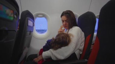 Genç çocuk, hava yoluyla seyahat ederken rahatlık ve etkileşim arayışında. Bakıcı, güven tazeleme ve ortak uçuş deneyimi sahnesi yaratarak tepki veriyor.