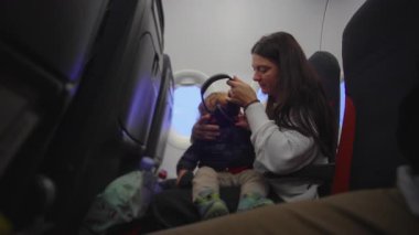 Bakıcı, uçak kabinindeki küçük çocuğa nazikçe kulaklık takar ve ayrılmadan önce rahatlama, dikkat çekme ve sessiz adaptasyon anı yaratır.