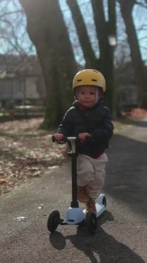 Küçük çocuk scooter 'ı ağaçlık yolda ileri itiyor. Bağımsızlığını ve sağlıklı aile yaşam tarzını ifade ediyor.