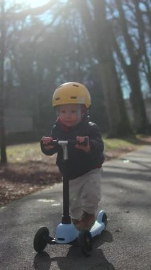 Genç çocuk uzun şortların altında asfalt yol boyunca süzülerek bağımsızlık koordinasyon merakını ve doğadaki aktif aile yaşam tarzını ifade eder.
