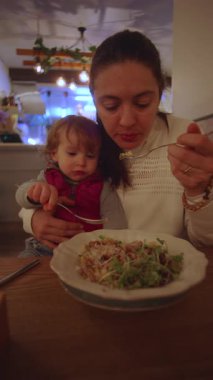 Ebeveynler kaşıkla çocuğu masada dengeleyerek, küçük çocukla olan sorumluluk bağlantısını ve modern yaşam tarzını yansıtır.