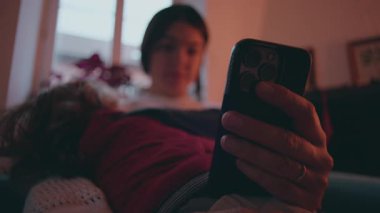 Çocuk göğsüne yaslanırken ebeveyn telefona sarılıyor. Bakım sorumluluğu ve aile içinde günlük gerginlik paylaşılıyor.