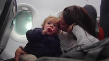 Ebeveyn, çocuğun uçak koltuğu kontrolleriyle etkileşimini izliyor. Havacılık ortamında rehberlik sabrı bağlanmasını ve modern ebeveynliği ifade ediyor.