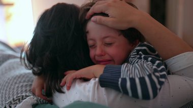 Anne ağlayan çocuğu duygusal kucaklamayla teselli eder, eller nazikçe tutar, sevgiyi, korumayı ve bakımı ifade eder, sıkıntı anında aile desteği, yakın çekim anı
