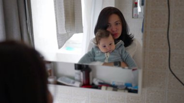 Anne banyodaki ayna yansıması, bağlanma anı, günlük rutin, aile zamanı, evde bakım, sabah bakımı, sevgi dolu etkileşimler.