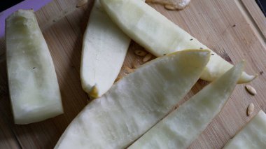 Ahşap kesim tahtasındaki kavun dilimleri, sulu meyve kalıntıları, dağınık tohumlar, taze kesilmiş parçalar, doğal dokular, sağlıklı atıştırma hazırlığı, kırsal mutfak sahnesi.