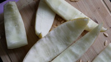 Ahşap kesim tahtasındaki kavun dilimleri, sulu meyve kalıntıları, dağınık tohumlar, taze kesilmiş parçalar, doğal dokular, sağlıklı atıştırma hazırlığı, kırsal mutfak sahnesi.