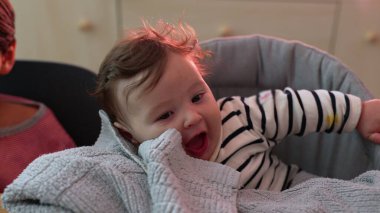 Yumuşak battaniyenin üzerinde eli ile gülümseyen bebeğe yakın çekim, neşeli ve neşeli yüz ifadesi, rahat bir şekilde oturup, çevreyle, yumuşak dokularla ve nazik anlarla meşgul olma