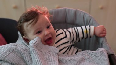 Yumuşak battaniyenin üzerinde eli ile gülümseyen bebeğe yakın çekim, neşeli ve neşeli yüz ifadesi, rahat bir şekilde oturup, çevreyle, yumuşak dokularla ve nazik anlarla meşgul olma