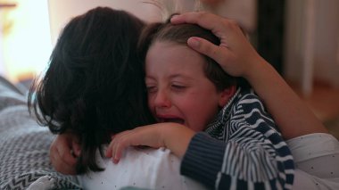Anne ağlayan çocuğu duygusal kucaklamayla teselli eder, eller nazikçe tutar, sevgiyi, korumayı ve bakımı ifade eder, sıkıntı anında aile desteği, yakın çekim anı