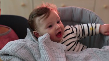 Yumuşak battaniyenin üzerinde eli ile gülümseyen bebeğe yakın çekim, neşeli ve neşeli yüz ifadesi, rahat bir şekilde oturup, çevreyle, yumuşak dokularla ve nazik anlarla meşgul olma