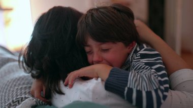 Anne ağlayan çocuğu duygusal kucaklamayla teselli eder, eller nazikçe tutar, sevgiyi, korumayı ve bakımı ifade eder, sıkıntı anında aile desteği, yakın çekim anı