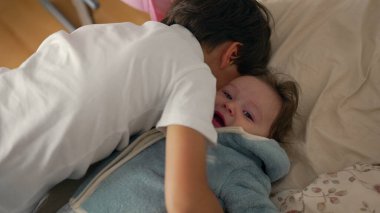 Genç çocuk yatakta bebeğe nazik bir öpücük veriyor, şefkat ve ilgi gösteriyor, kardeş şefkati gösteriyor, sıcak ve samimi, aile sevgisi ve bağ kurma, yumuşak ifade