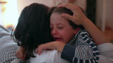 Anne ağlayan çocuğu duygusal kucaklamayla teselli eder, eller nazikçe tutar, sevgiyi, korumayı ve bakımı ifade eder, sıkıntı anında aile desteği, yakın çekim anı