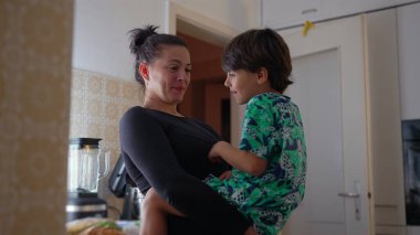 Anne oğlunu mutfakta tutuyor, neşeli bir sohbete girişiyor, yakın bir bağ kuruyor, ebeveynle çocuk arasında sevgi dolu bir an, sıcak bir ev ortamı yaratıyor.