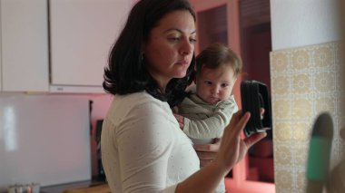 Anne, bebeğini mutfakta tutarken, ev işlerini düzenlerken ve yönetirken, ebeveynliğe ve aile ortamını geliştirmeye odaklanırken,