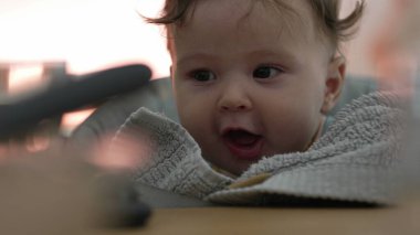 Bebek masadaki dokulu kumaşa dokunmak için uzanıyor, elleriyle keşfediyor, duyusal gelişime odaklanıyor, yüksek sandalyede otururken dokunsal oyunlara odaklanıyor.