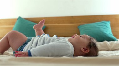 Bebek mutlu bir gülümseme ile ayaklarına uzanır, merak ve neşe ifade eder, rahat bir aile ortamında çocukluk zamanlarının neşeli ve tasasız anlarını yakalar.